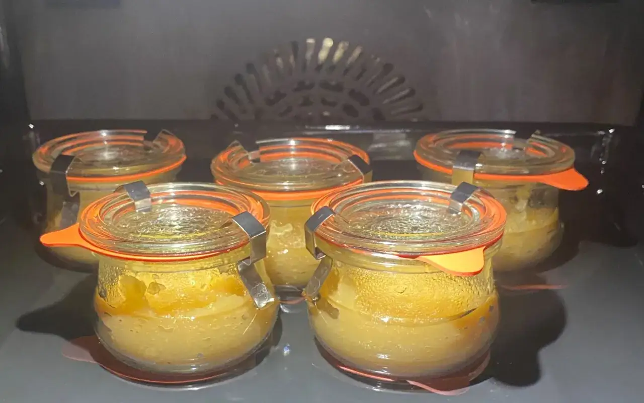 F&uuml;nf Gl&auml;ser mit Apfelmus im Backofen einkochen. Die Gl&auml;ser sind mit orangefarbenen Dichtungen und silbernen Klammern verschlossen.