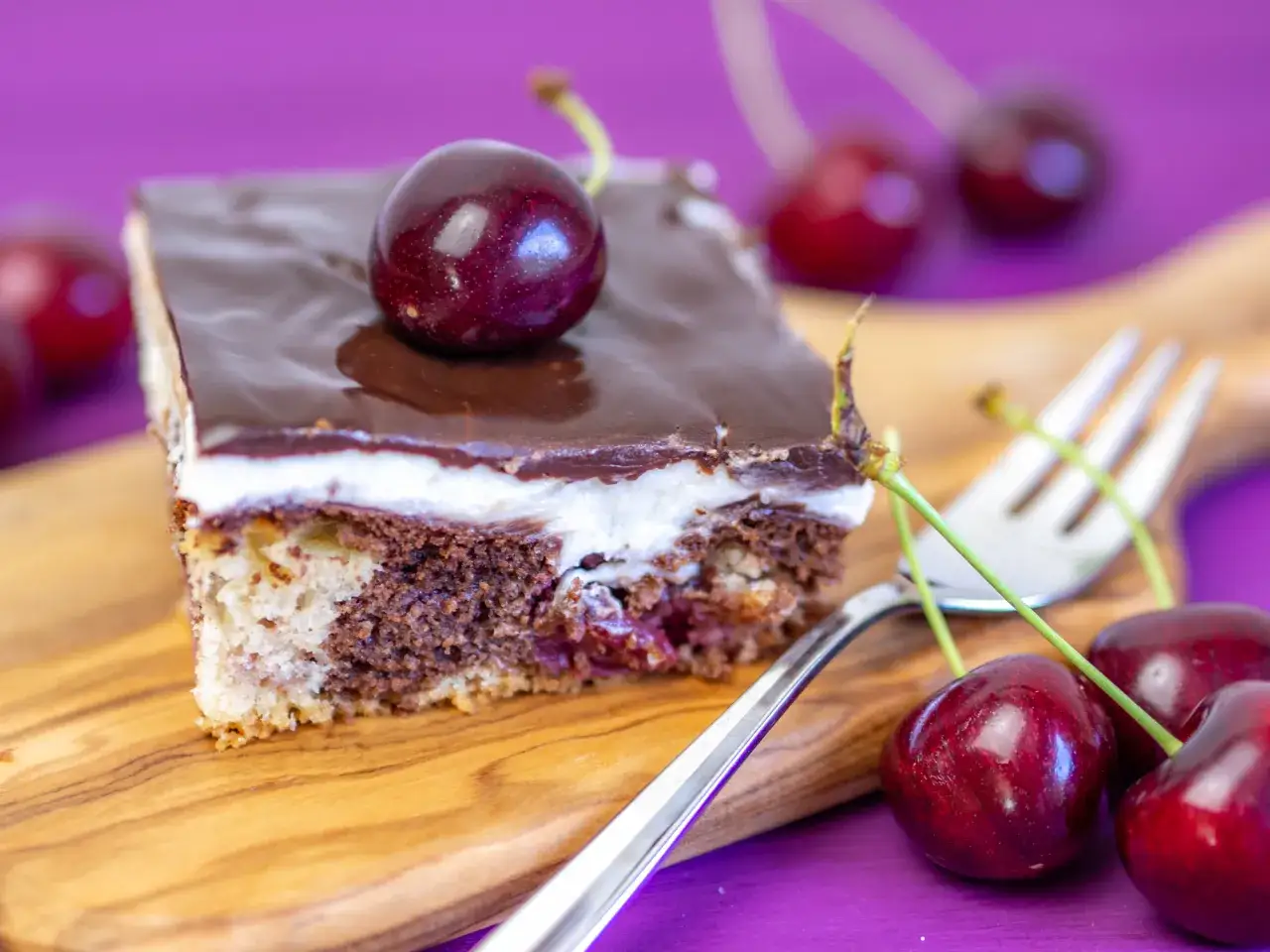 Ein Stück Donauwelle Kuchen mit Schokoglasur, Sahne und Kirschen, bereit zum Genießen. Ein köstliches Donauwelle Rezept.