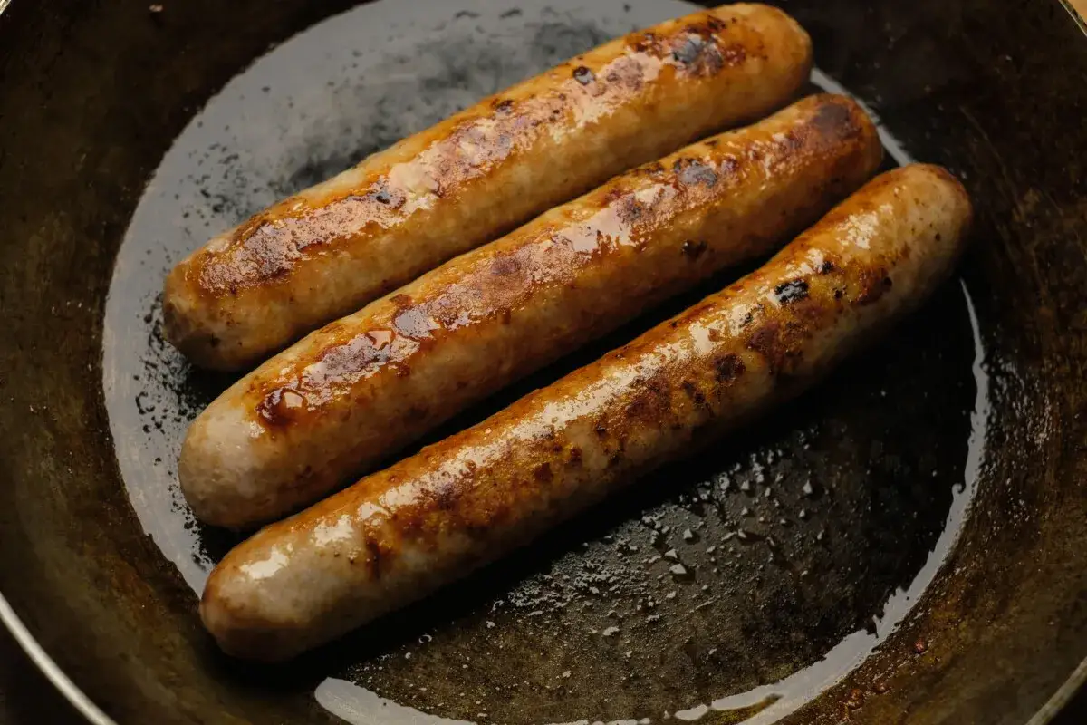 Drei goldbraune bratwurst in der pfanne, die in ihrem eigenen Saft brutzeln.