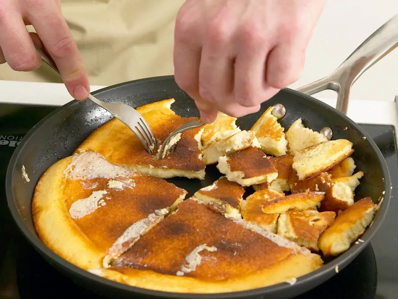 Zwei Gabeln zerreißen einen goldbraunen Kaiserschmarrn in einer Pfanne. Ein leckeres Kaiserschmarrn Rezept zum Nachmachen!