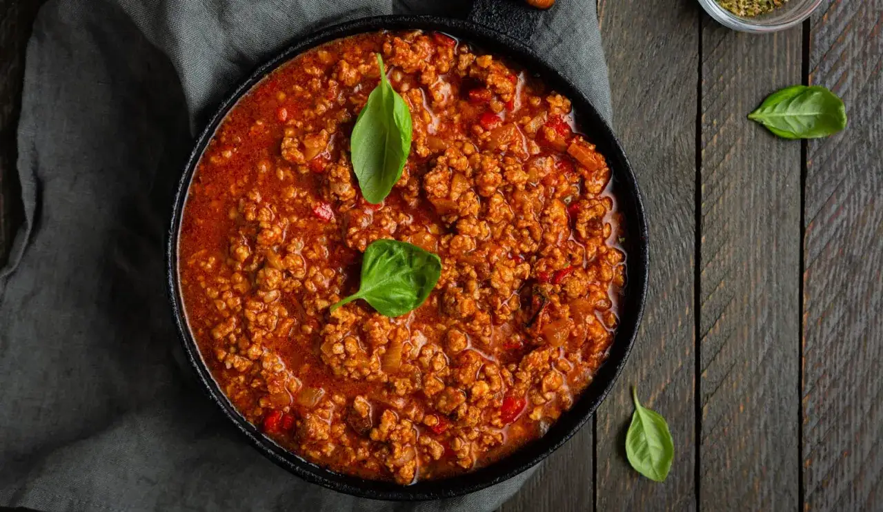 Herzhafte Bolognese-Sauce in einem schwarzen Dutch Oven, garniert mit frischem Basilikum.