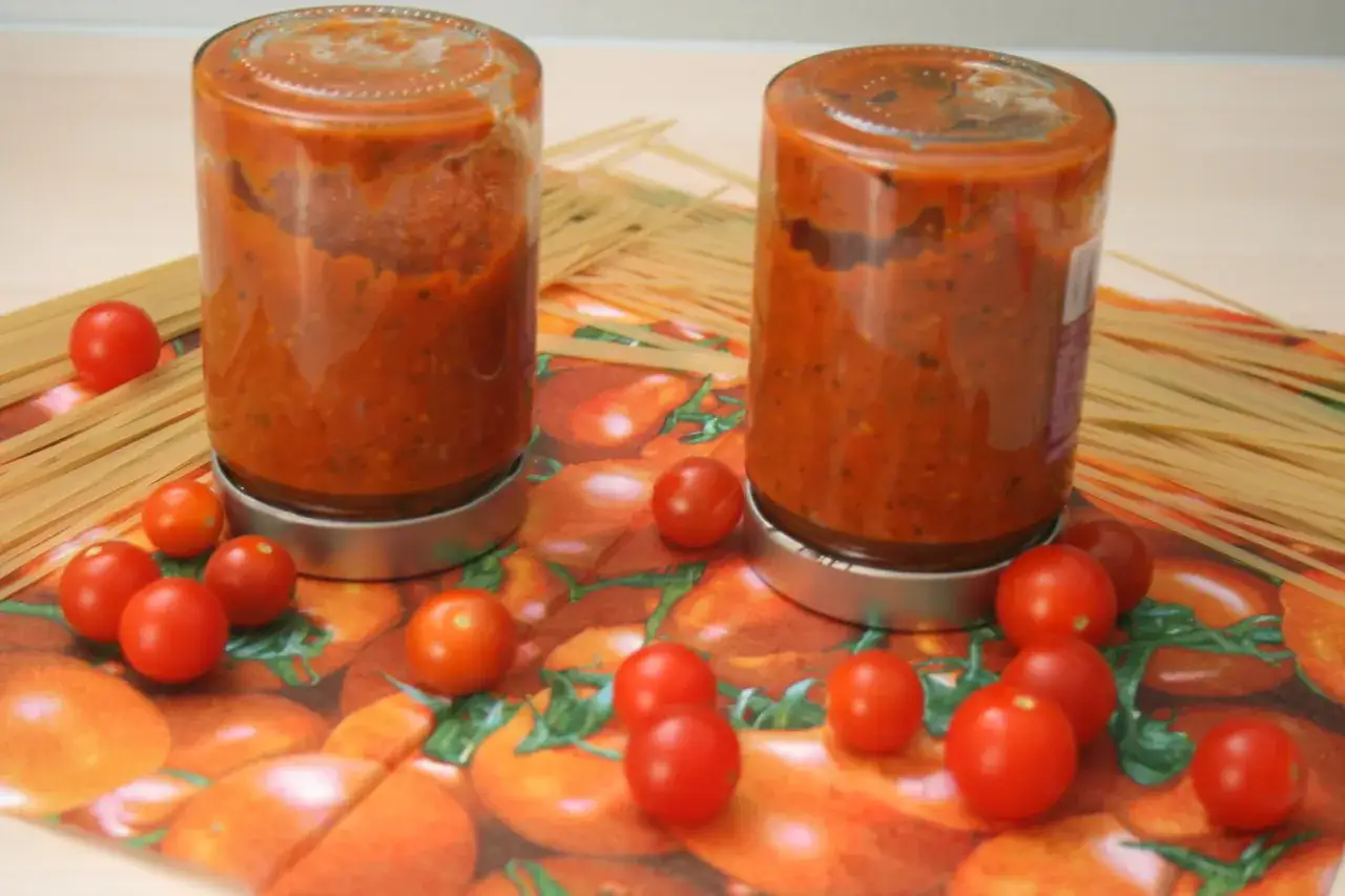 Zwei Gl&auml;ser mit Tomatenso&szlig;e, umgeben von frischen Tomaten und Spaghetti. Perfekt f&uuml;r die Tomaten haltbar machen.