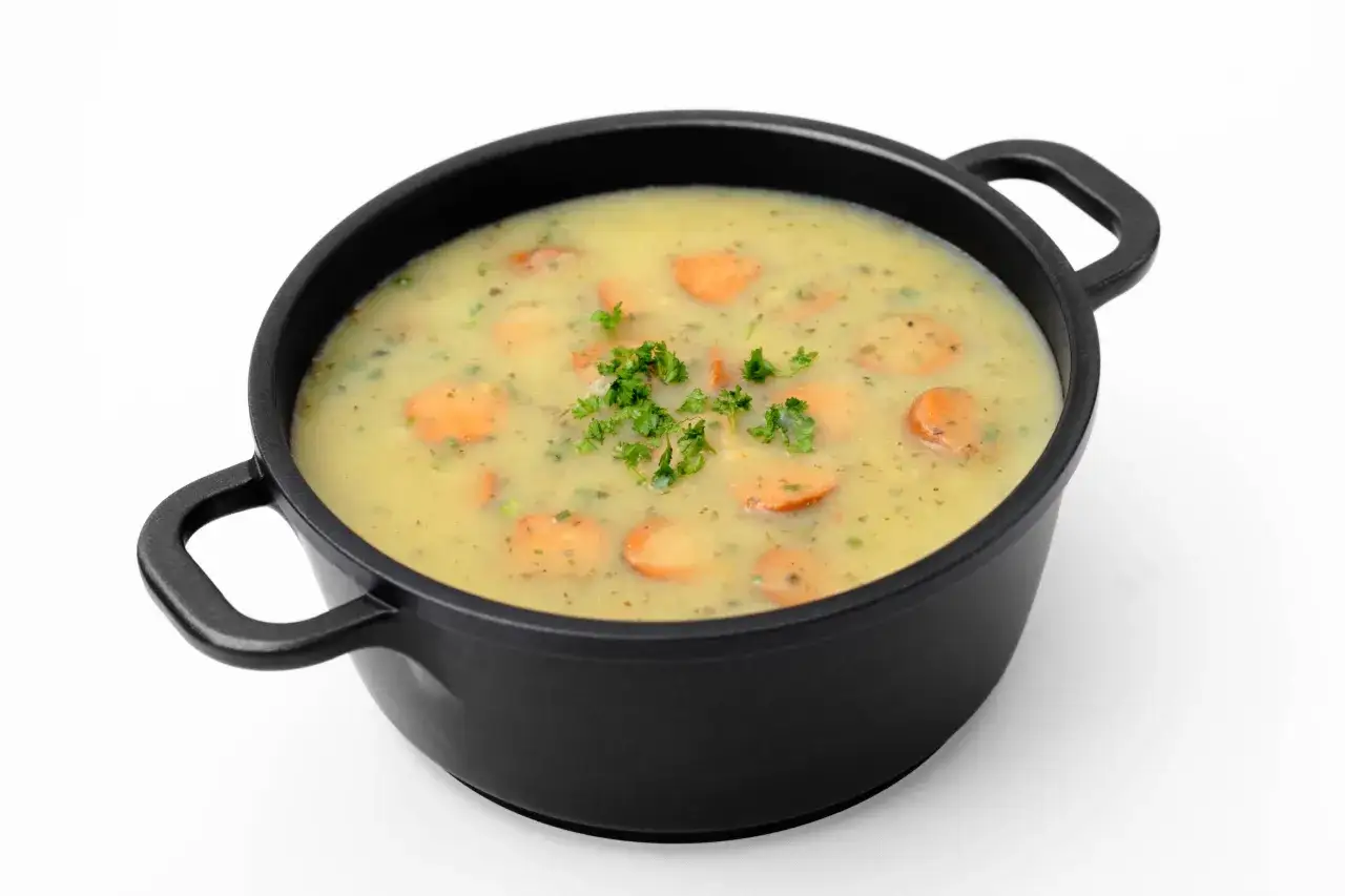 Eine cremige Gem&uuml;sesuppe mit Karottenscheiben und Petersilie in einem schwarzen Topf, wie aus Omas Rezepten f&uuml;r das Mittagessen.