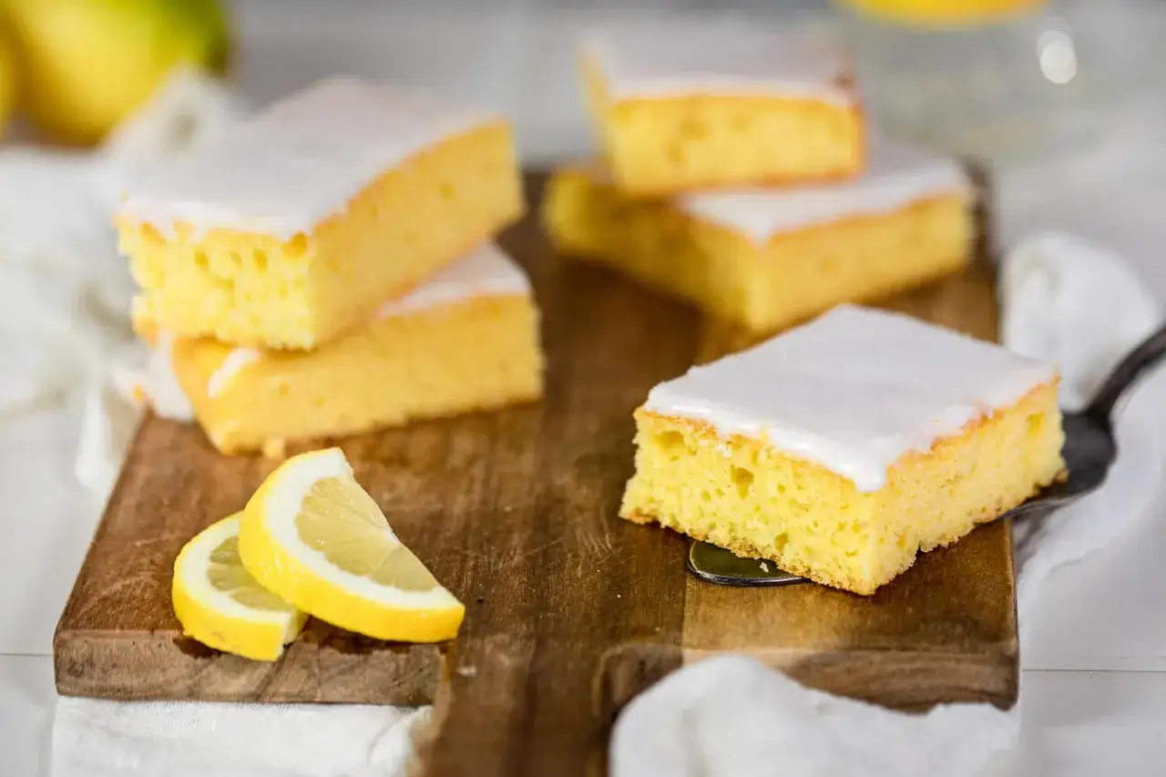 Saftiger Omas Zitronenkuchen vom Blech, mit zarter Glasur und frischen Zitronenspalten auf einem Holzbrett.