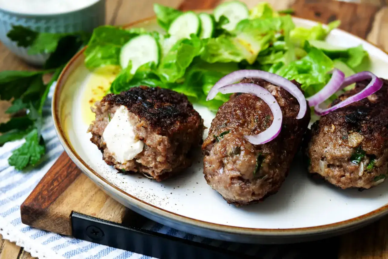 Saftige Bifteki, gef&uuml;llt mit K&auml;se, serviert mit Salat und Zwiebelringen. Ein k&ouml;stliches Bifteki Rezept zum Nachkochen.
