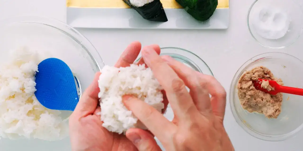 H&auml;nde formen Reis zu einem Ball, um Onigiri selber zu machen. Daneben Sch&uuml;ssel mit Thunfischf&uuml;llung und Salz.