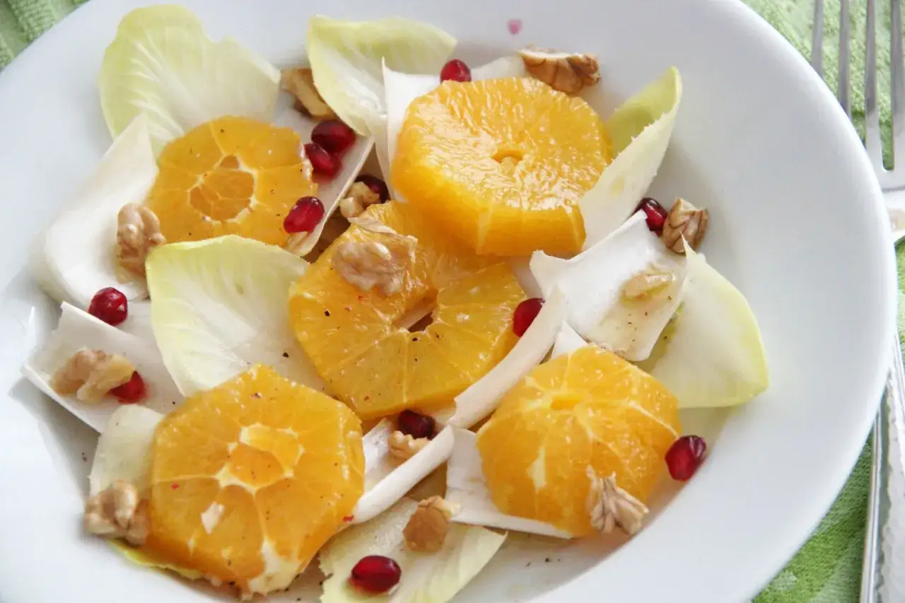 Erfrischender Chicorée-Salat mit saftigen Orangenspalten, knackigen Walnüssen und Granatapfelkernen auf einem weißen Teller.