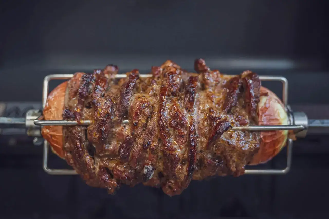 Saftiges Gyros vom Grill dreht sich auf einem Spie&szlig;, umgeben von einer gro&szlig;en Zwiebel.
