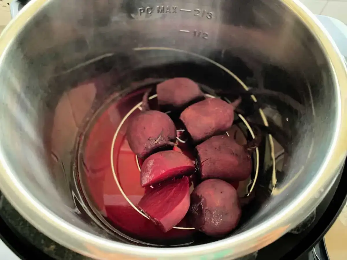 Rote Bete Kochzeit im Schnellkochtopf. Ganze und geschnittene Rote Bete liegen auf einem Einsatz in rotem Wasser.