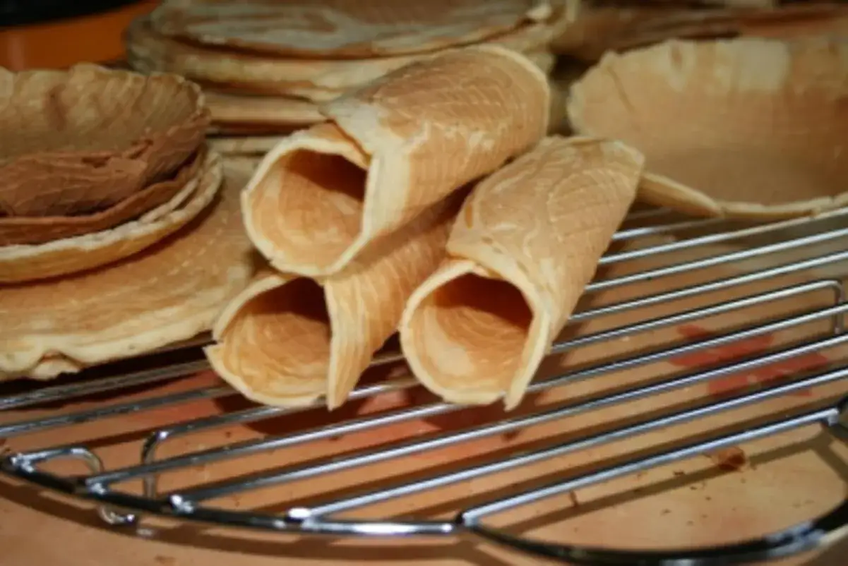 Omas Neujahrskuchen Rezept: Frisch gebackene, goldbraune Kekse in R&ouml;llchenform und flache Waffeln liegen auf einem Gitter.