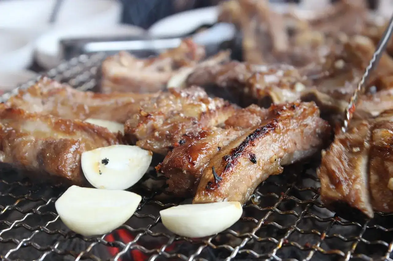 Saftige Spareribs grillen &uuml;ber Holzkohle, mit Knoblauchst&uuml;cken. Der Duft von gegrilltem Fleisch liegt in der Luft.