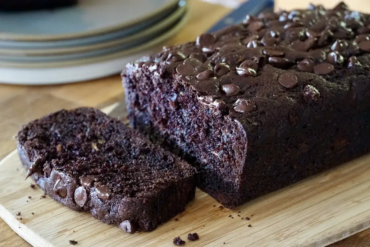Saftiger zucchini schoko kuchen mit Schokostückchen, frisch gebacken und auf einem Holzbrett angerichtet.
