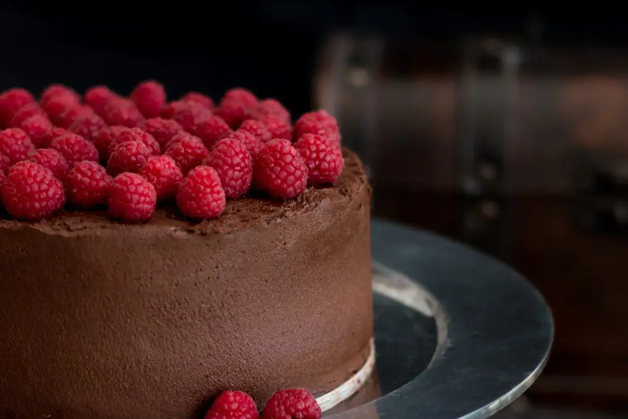 Schokokuchen rezept: Ein saftiger Schokoladenkuchen, &uuml;ppig mit frischen Himbeeren belegt, auf einer silbernen Platte.