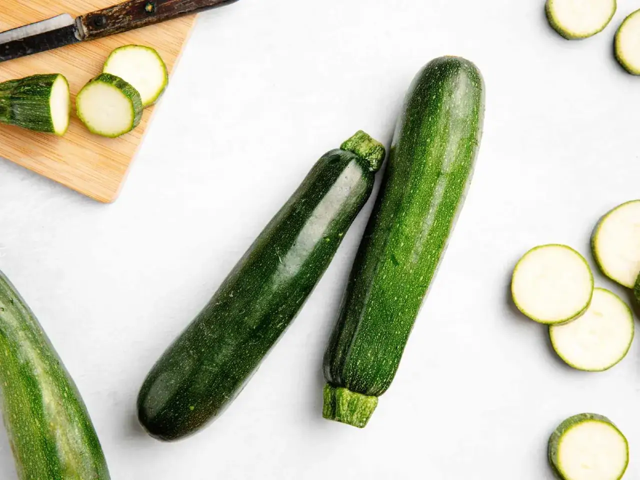 Zwei frische Zucchini liegen neben geschnittenen Scheiben. Ja, kann man Zucchini mit Schale essen!