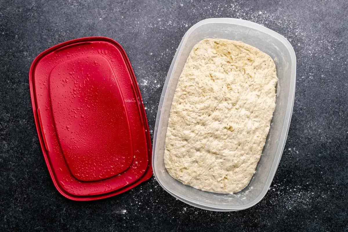 Pizzateig ruht im Kühlschrank, bereit, um den pizzateig am vortag machen zu können. Der rote Deckel liegt daneben.