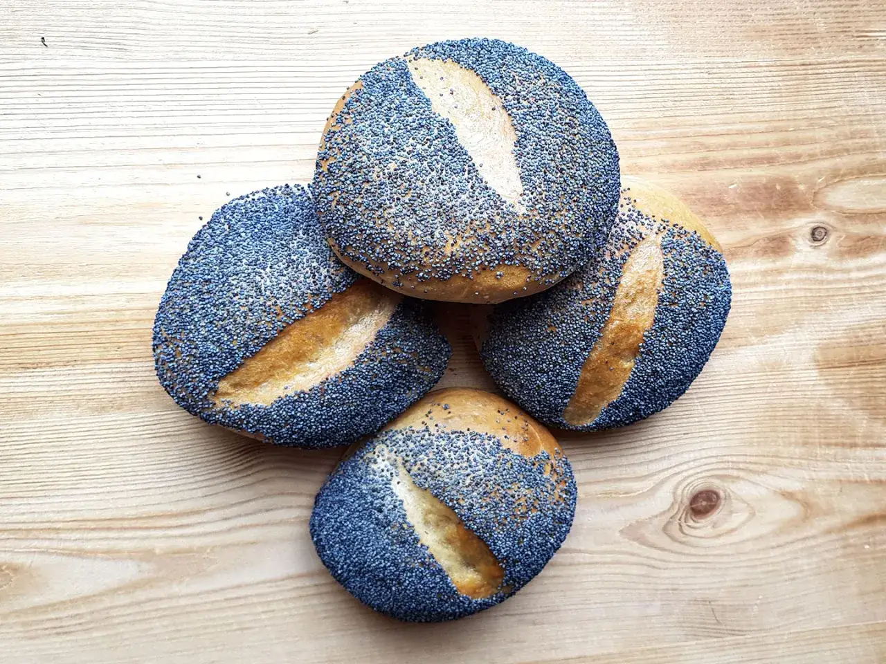 Vier Mohnbr&ouml;tchen liegen auf einem Holztisch. Sind Mohnbr&ouml;tchen gesund? Ja, Mohn ist reich an N&auml;hrstoffen.