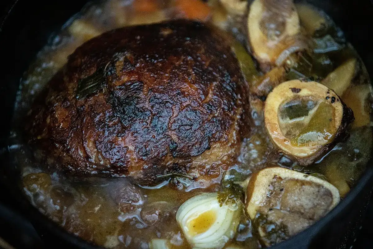 Ein Tafelspitz gart langsam im Dutch Oven mit Knochenmark, Zwiebeln und Kr&auml;utern in einer k&ouml;stlichen Br&uuml;he.