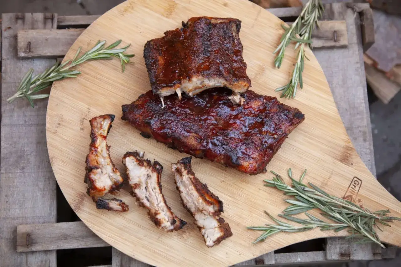 Saftige BBQ-Rippchen, bereit zum Genie&szlig;en. 3, 2, 1... rippchen! Rosmarin garniert das Holzbrett.