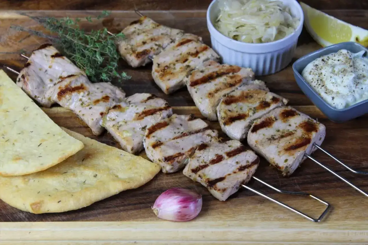Gegrillte Schweinefleisch-Souvlaki auf Spießen, serviert mit Fladenbrot, Krautsalat und Tzatziki. Welches Fleisch ist das?
