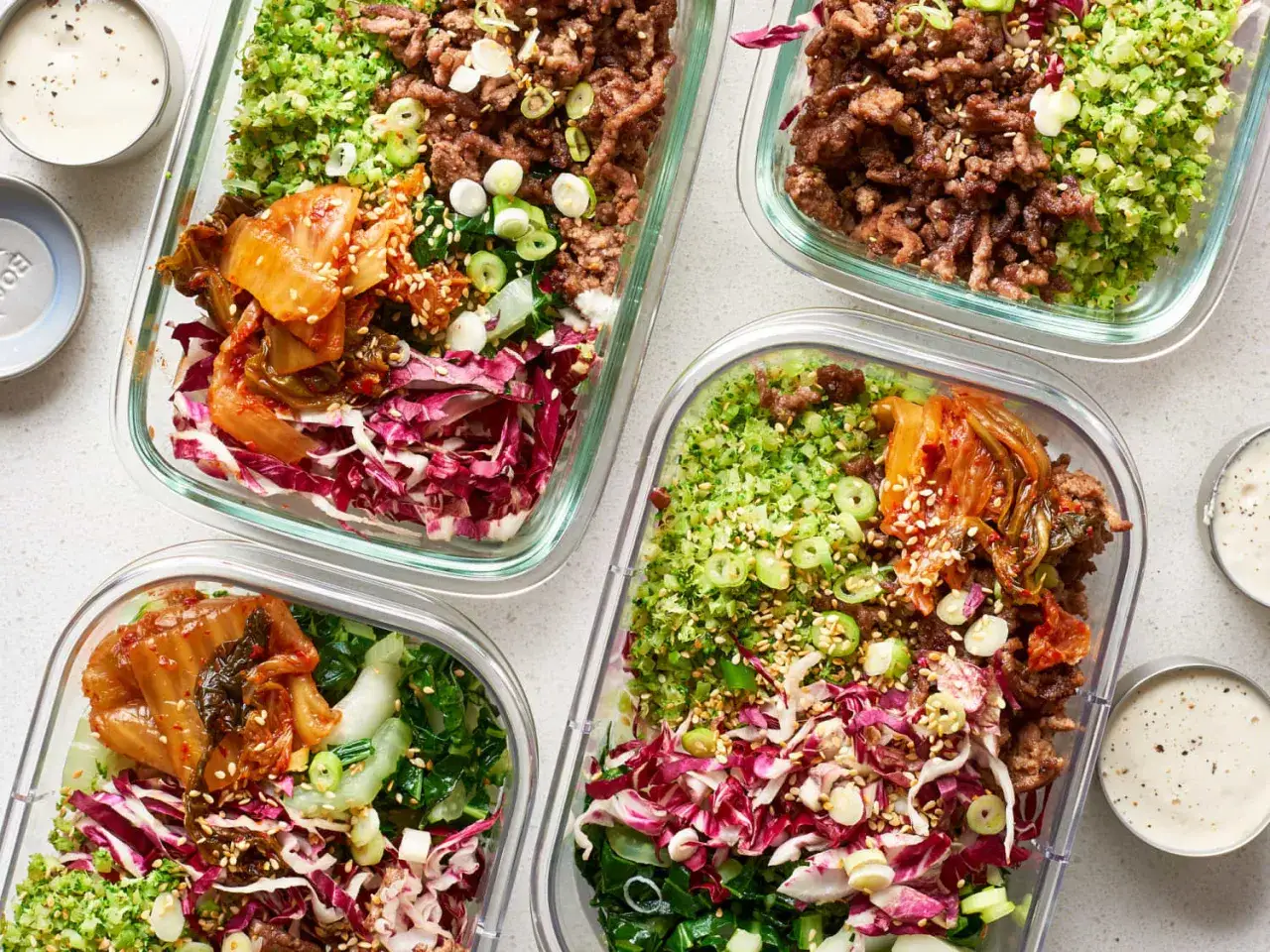 Vier Beh&auml;lter mit leckeren slow carb rezepten: Hackfleisch, Brokkoli-Reis, Kimchi und Rotkohl. Dazu kleine Sch&auml;lchen mit Dip.