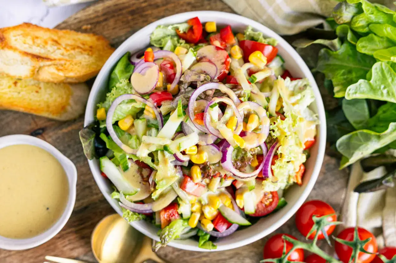 Ein bunter gemischter Salat mit knackigem Salat, Tomaten, Gurken, Mais und roten Zwiebeln, serviert mit Dressing und ger&ouml;stetem Brot.