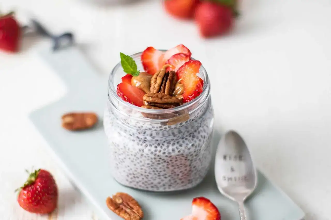 Ein Glas cremiges Keto Chia Pudding mit Erdbeeren, Pekannüssen und Mandelbutter. Perfekt für einen gesunden Start in den Tag.