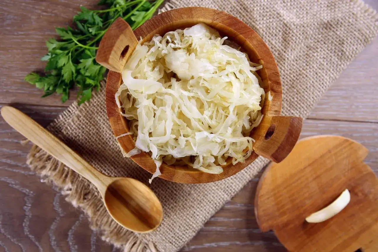 Frisches Sauerkraut in einer Holzschale, bereit f&uuml;r ein leckeres Sauerkraut Rezept. Dazu Petersilie und ein Holzl&ouml;ffel.