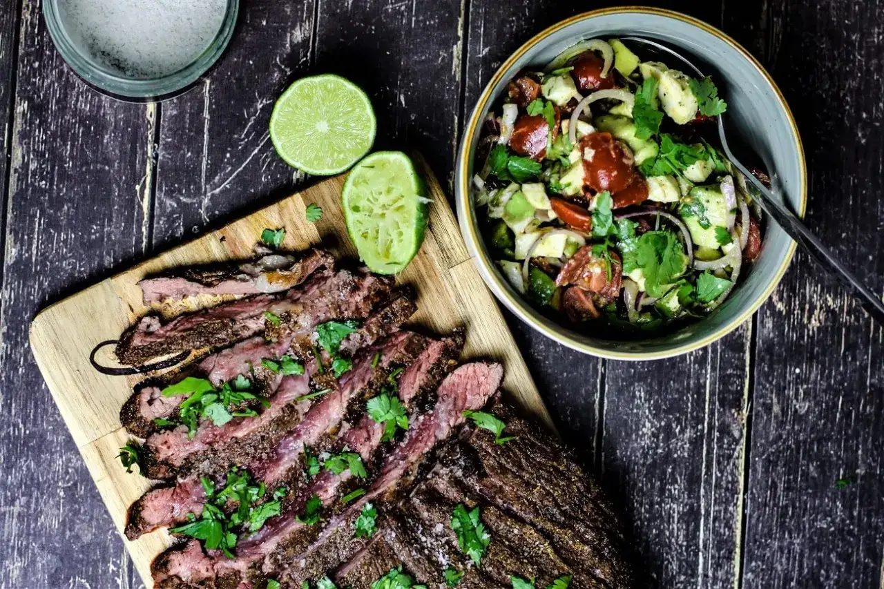 Perfekt gegrilltes Flank Steak, geschnitten und mit Koriander bestreut, neben einem frischen Avocado-Tomaten-Salat. Ein tolles Flank Steak Rezept f&uuml;r den Sommer.