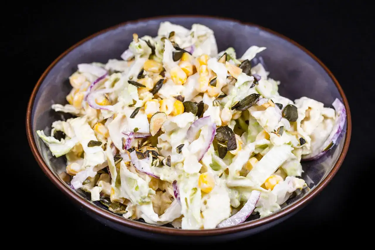 Ein cremiger Chinakohlsalat mit Mais, roten Zwiebeln und K&uuml;rbiskernen, garniert mit Kr&auml;utern.
