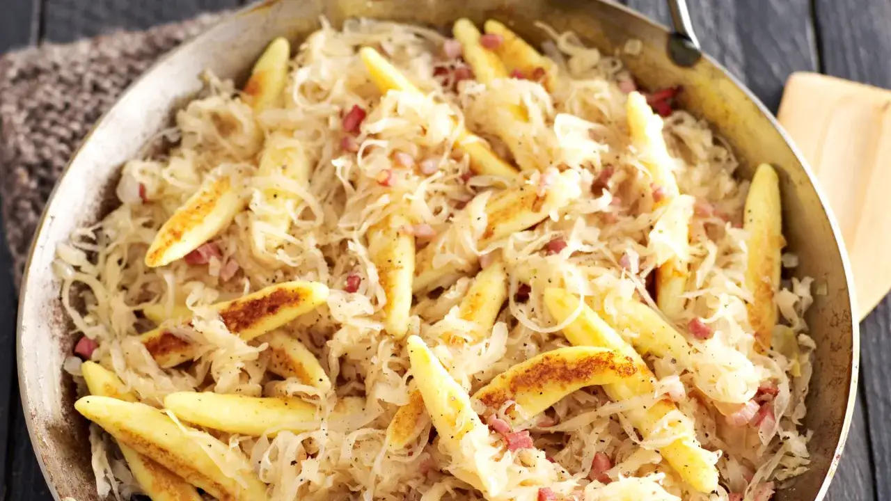 Schupfnudeln mit Sauerkraut und Speckw&uuml;rfeln in einer Pfanne, ein herzhaftes Gericht.