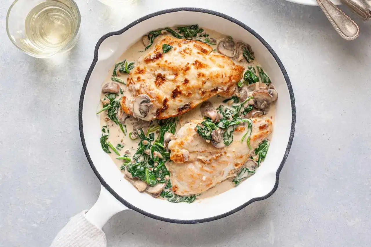 Zwei gebratene H&auml;hnchenbrustfilets in cremiger Pilz-Spinat-Sauce in einer Pfanne. Ein leckeres und schnelles Gericht f&uuml;r jeden Tag.