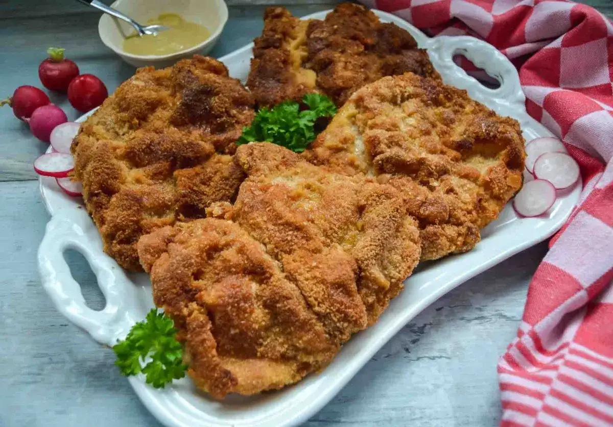 Goldbraune Schnitzel auf einer Platte, perfekt paniert. Die richtige Schnitzel panieren Reihenfolge macht den Unterschied f&uuml;r diese knusprige K&ouml;stlichkeit. Beilage: Radieschen und Petersilie.