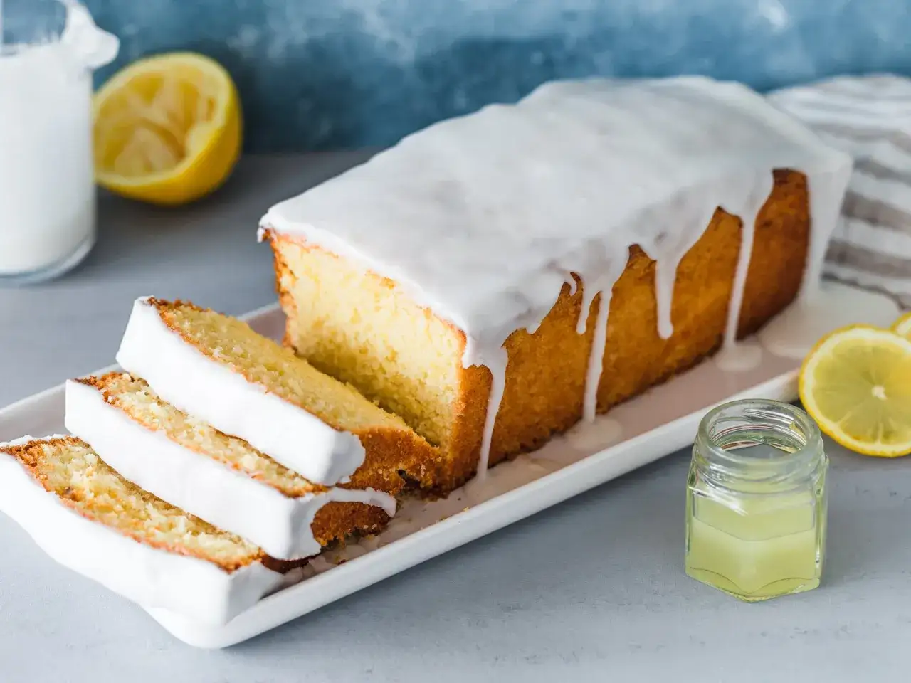 Ein saftiger Zitronenkuchen mit Zuckerguss, der aussieht wie der beste Zitronenkuchen der Welt. Daneben liegen Zitronenscheiben und ein kleines Glas Zitronensaft.