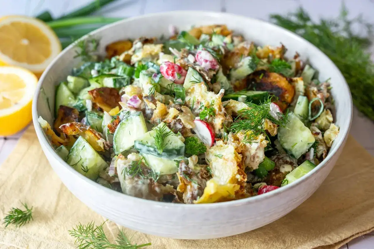 Herzhafter smashed potato salat mit Gurken, Radieschen und Dill in einer Sch&uuml;ssel, garniert mit Zitrone.