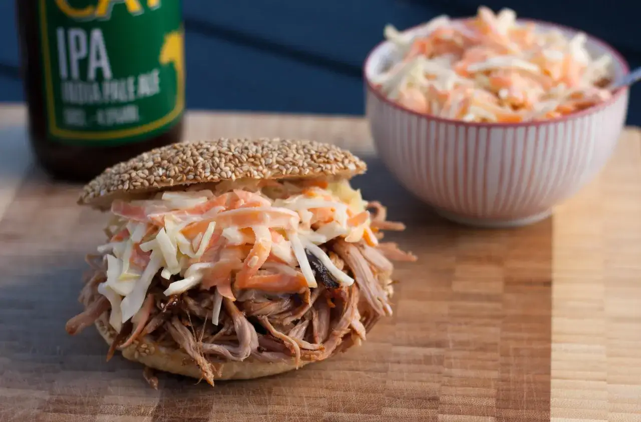 Pulled Pork Sandwich mit Coleslaw, perfekt f&uuml;r ein schnelles pulled pork rezept. Daneben eine Sch&uuml;ssel mit Coleslaw und eine IPA-Flasche.