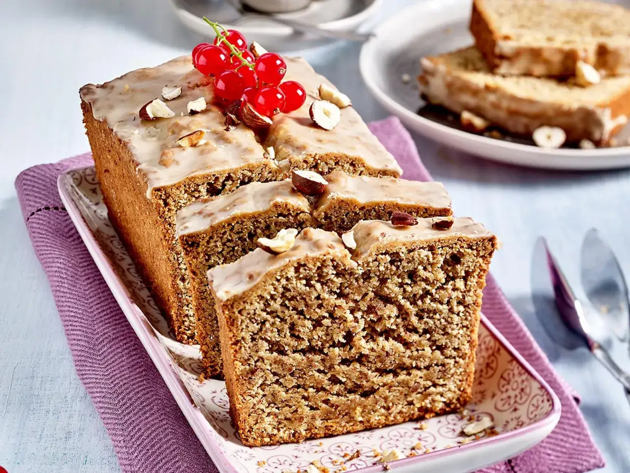 Saftiger Kuchen ohne Mehl, verziert mit Zuckerguss, N&uuml;ssen und roten Johannisbeeren.