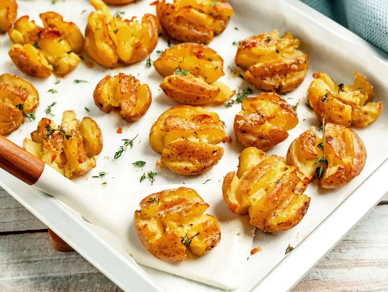 Knusprig gebackene, zerdr&uuml;ckte Kartoffeln mit Kr&auml;utern und Gew&uuml;rzen auf einem Backblech.