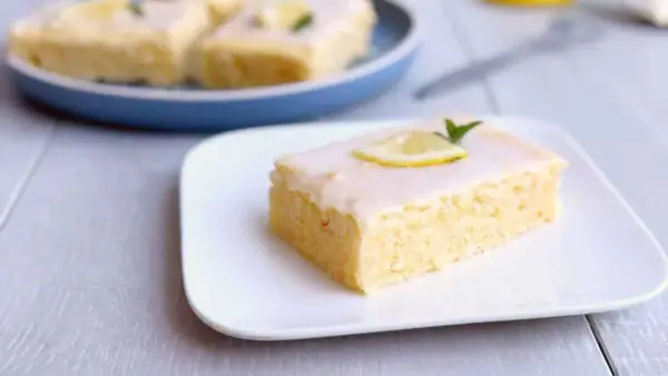 Ein Stück von Omas Zitronenkuchen vom Blech, mit Zuckerguss und Zitronenscheibe garniert.