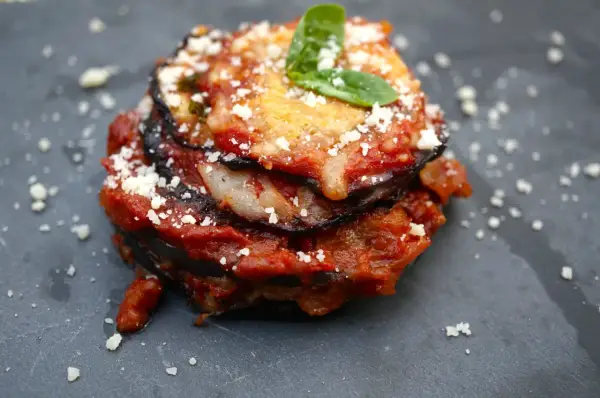 Melanzane alla Parmigiana: geschichtete Aubergine mit Tomatensauce, Käse und Basilikum, bestreut mit Parmesan.