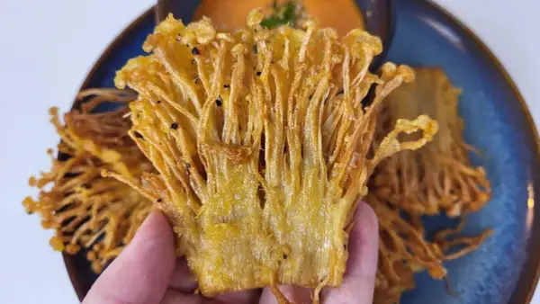 Knusprige Enoki Pilze, perfekt für ein einfaches enoki pilze rezept. Goldbraun frittiert und auf einem blauen Teller serviert.