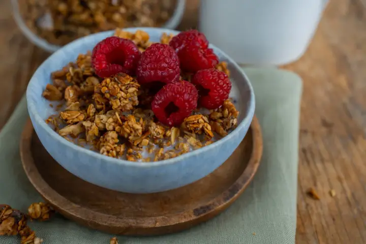 Schüssel mit selbstgemachtem Granola, Milch und frischen Himbeeren. Ein gesunder Start in den Tag!